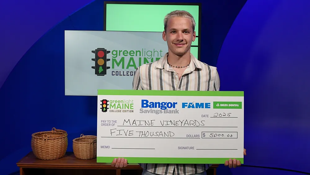 Thomas College student Zephyr Lani-Caputo holds winning check in Greenlight Maine studio