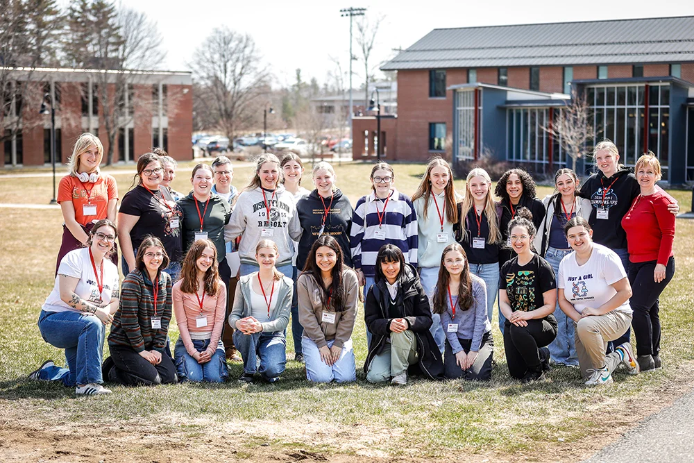 A group of high school students and Thomas College students pose together outside with the campus buildings in the background during Girls in Science Day at Thomas College