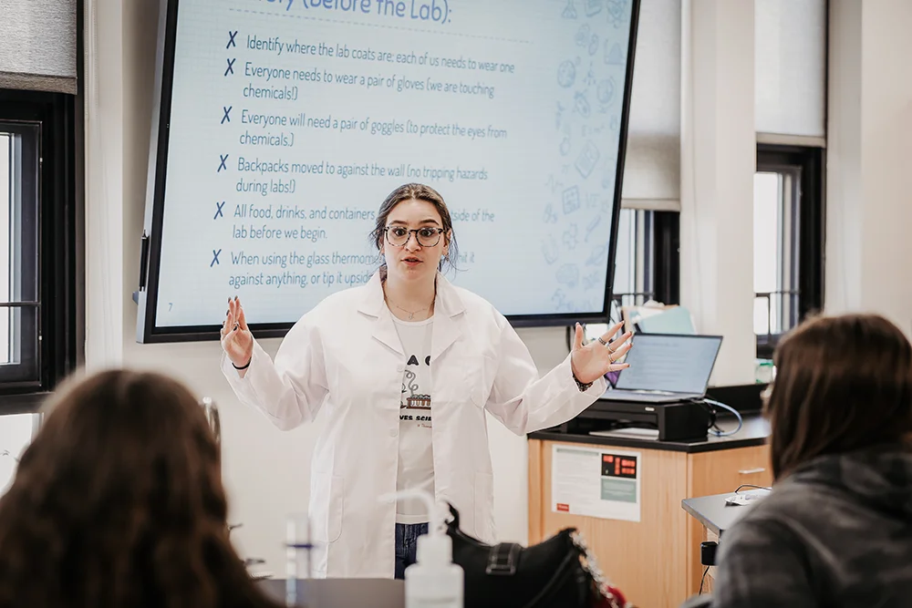 Thomas student Sophie Damon instructs her group of high school students in the science lab at Thomas College during Girls in Science Day