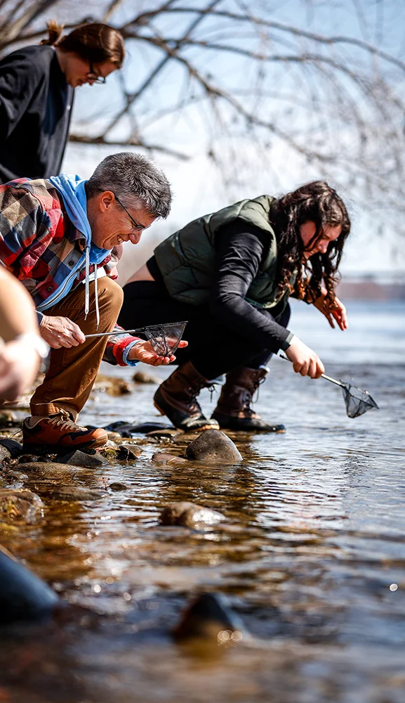 Tess Harden and a group of students work at the edge of the Kennebec River during Girls in Science Day