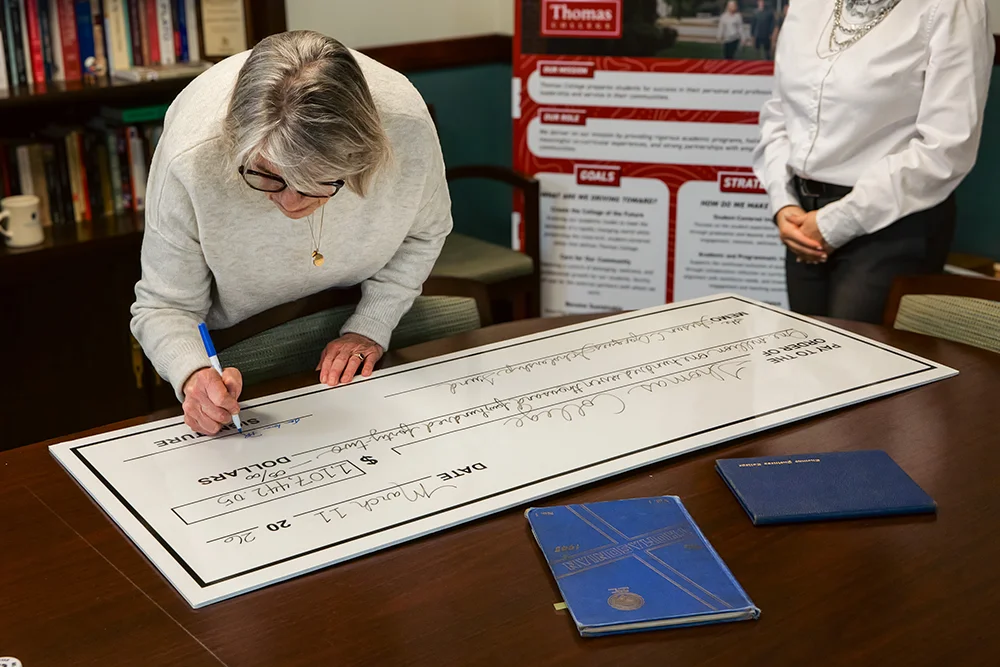 Laurah Brown signing the check at Thomas College for the Susan C. Jacques Scholarship Fund