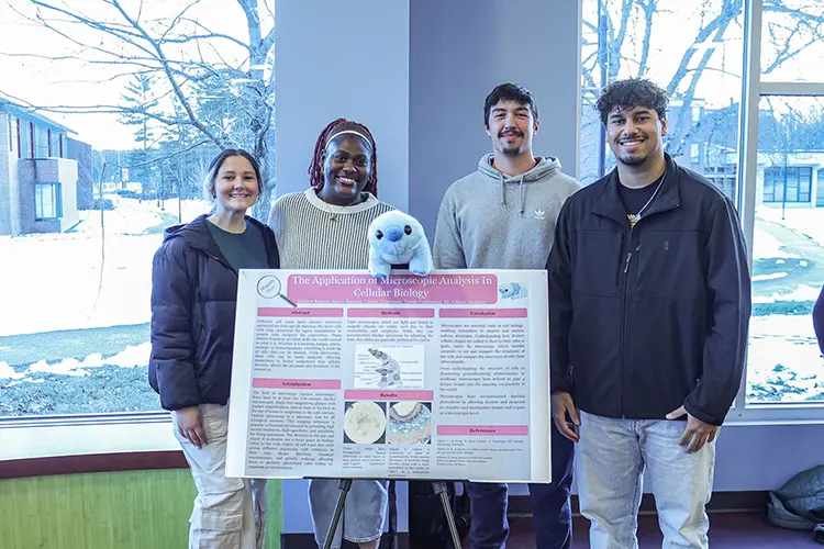 Thomas College student Alexis Spencer stands with three other students in front of a poster during the Academic Symposium