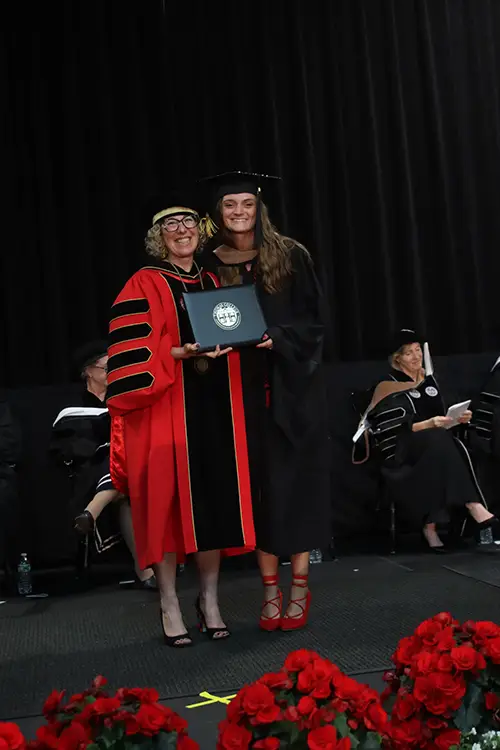 Terrier STAR and staff member Mariena Bragg stands on the Commencement stage at Thomas College with President Uzzi