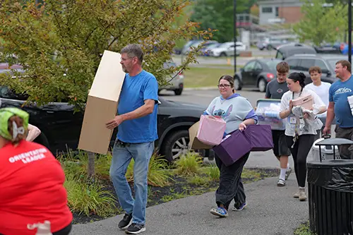 An entering student and their family holding items to move into a residence hall
