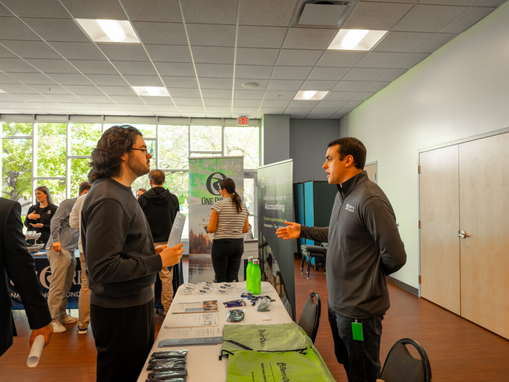 A Thomas College student stands to the left listening to the accounting staff member on the right during accounting firm night